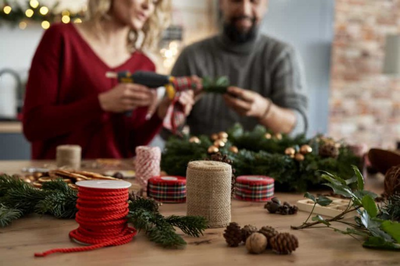 table full of christmas decorations and couple making christmas wreath 1024x682